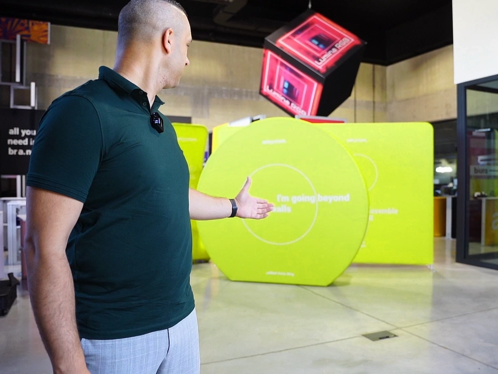 Una persona señala un photocall circular Vario Q-anillo de color verde instalado en un showroom, mostrando su diseño redondo y moderno ideal para destacar en presentaciones o eventos.