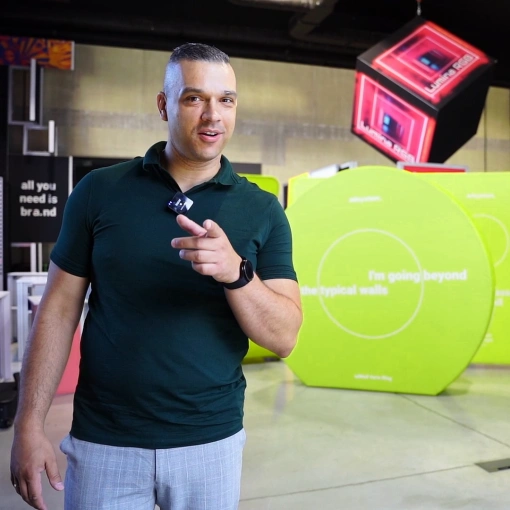 file-meta-description.mężczyznawzielonejkoszulcewskazujewstronękamery,stojącnatlekolorowychsystemówwystawienniczych.