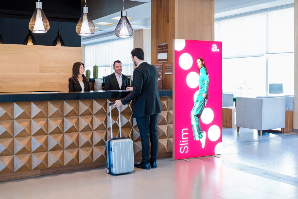 Kaseton reklamowy Slim ustawiony przy recepcji hotelowej jako nośnik przyciągającej wzrok komunikacji wizualnej.