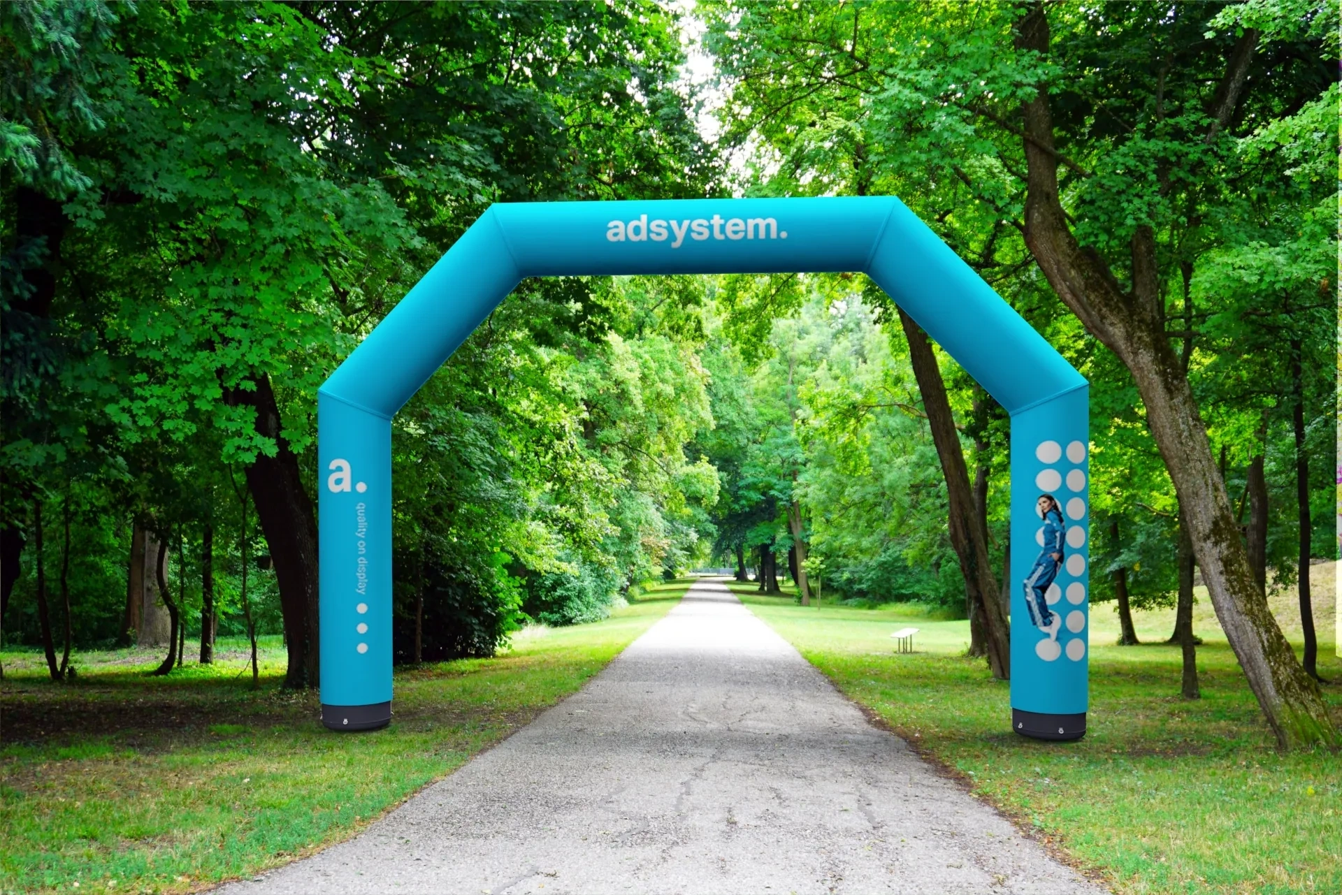 Niebieska pneumatyczna brama reklamowa ustawiona na leśnej alejce, otoczona zielonymi drzewami.