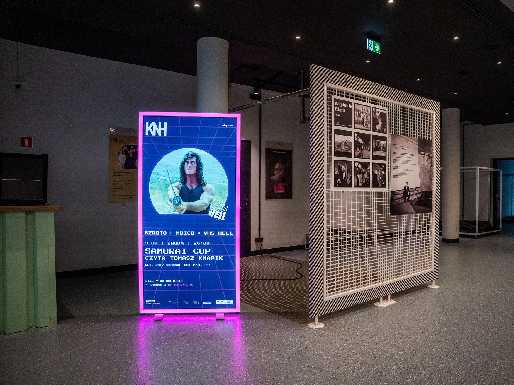 Zdjęcie przedstawia podświetlany kaseton reklamowy adsystem z grafiką promującą film Samurai Cop, ustawiony w przestrzeni wystawienniczej Kina Nowe Horyzonty.