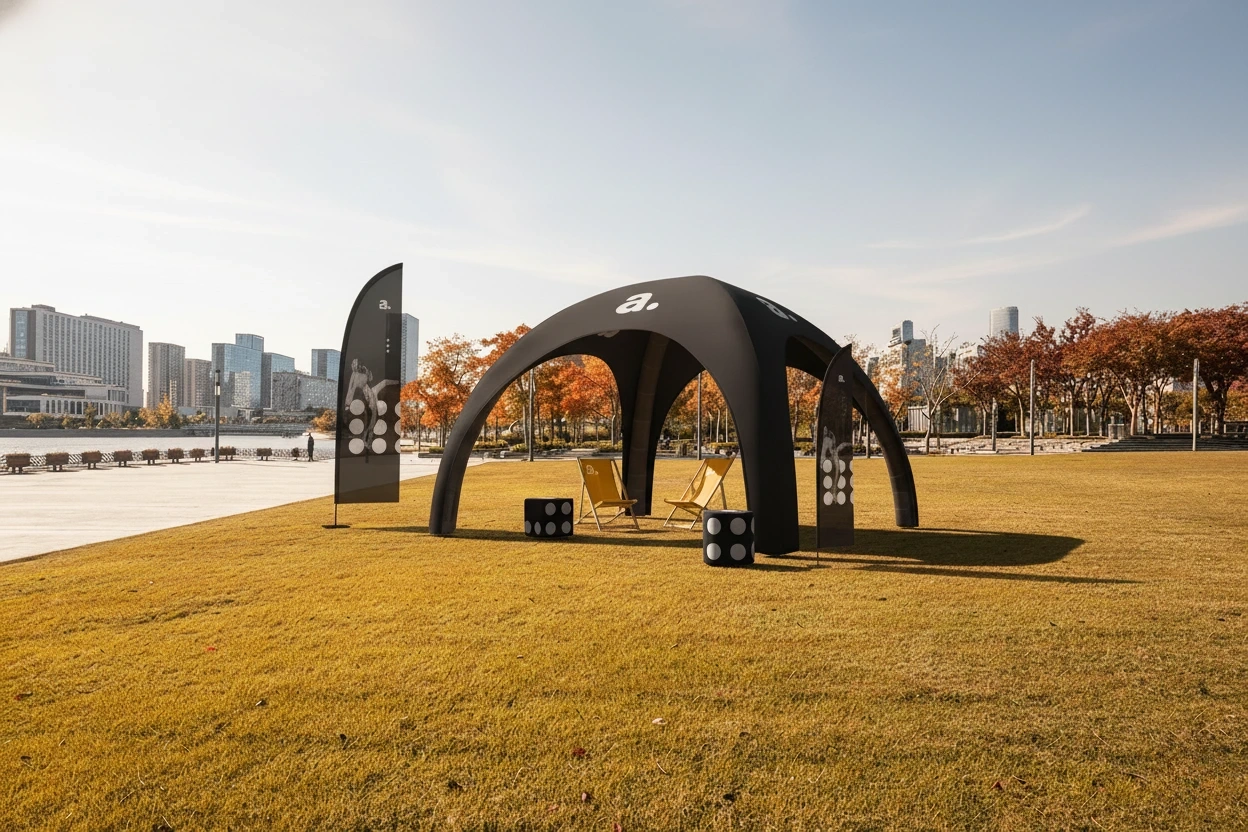 Czarny nadmuchiwany namiot eventowy z flagami reklamowymi i leżakami, ustawiony na jesiennym trawniku z panoramą miasta.