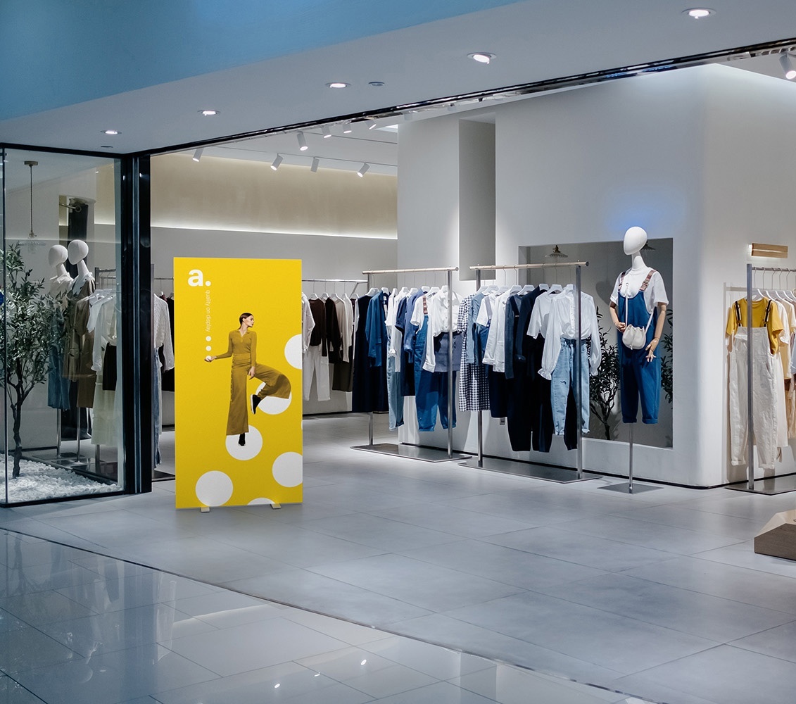 Kolorowy kaseton reklamowy z grafiką modową ustawiony przed eleganckim butikiem odzieżowym w centrum handlowym