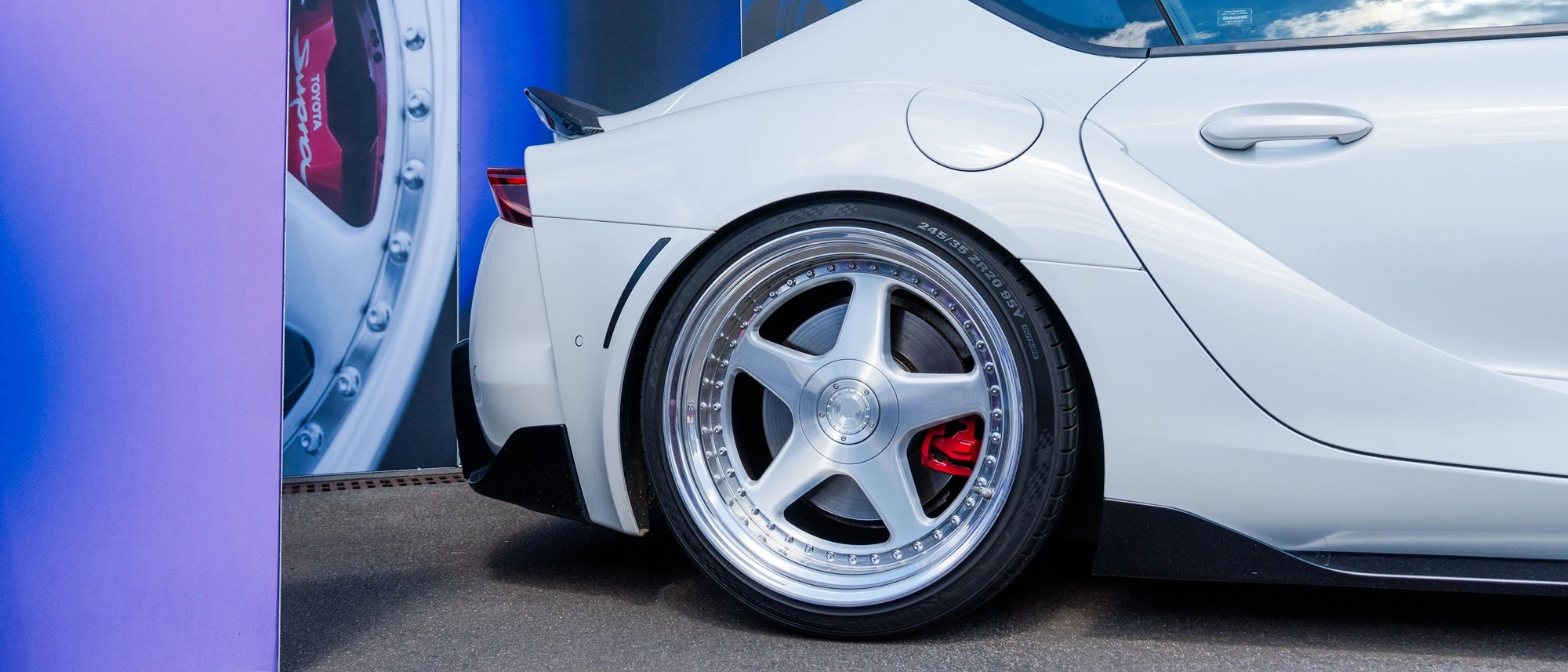 Zbliżenie na tylną część białej Toyoty Supra z felgą pięcioramienną i czerwonym zaciskiem hamulcowym, prezentowanej na stoisku adsystem podczas Ultrace 2025.