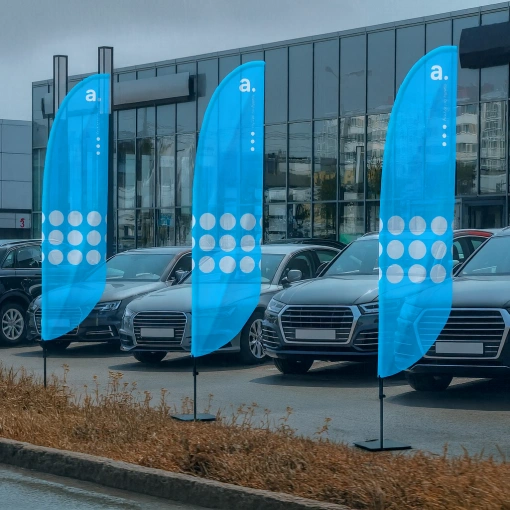 Bandeiras publicitárias azuis com logótipo adsystem colocadas em frente a um concessionário automóvel
