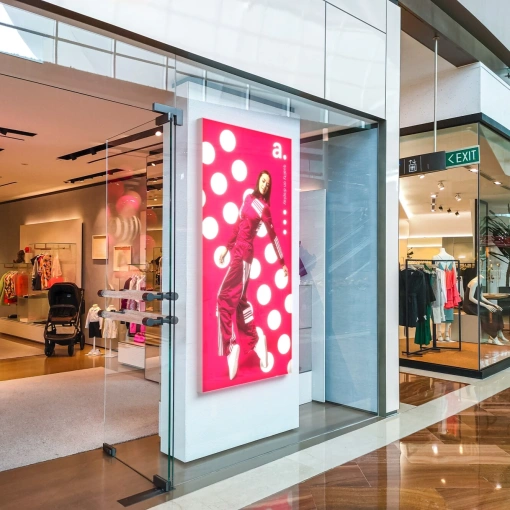 Caixa de luz LED com publicidade de moda à entrada de uma loja num centro comercial moderno, com interior e exposição de produtos visíveis