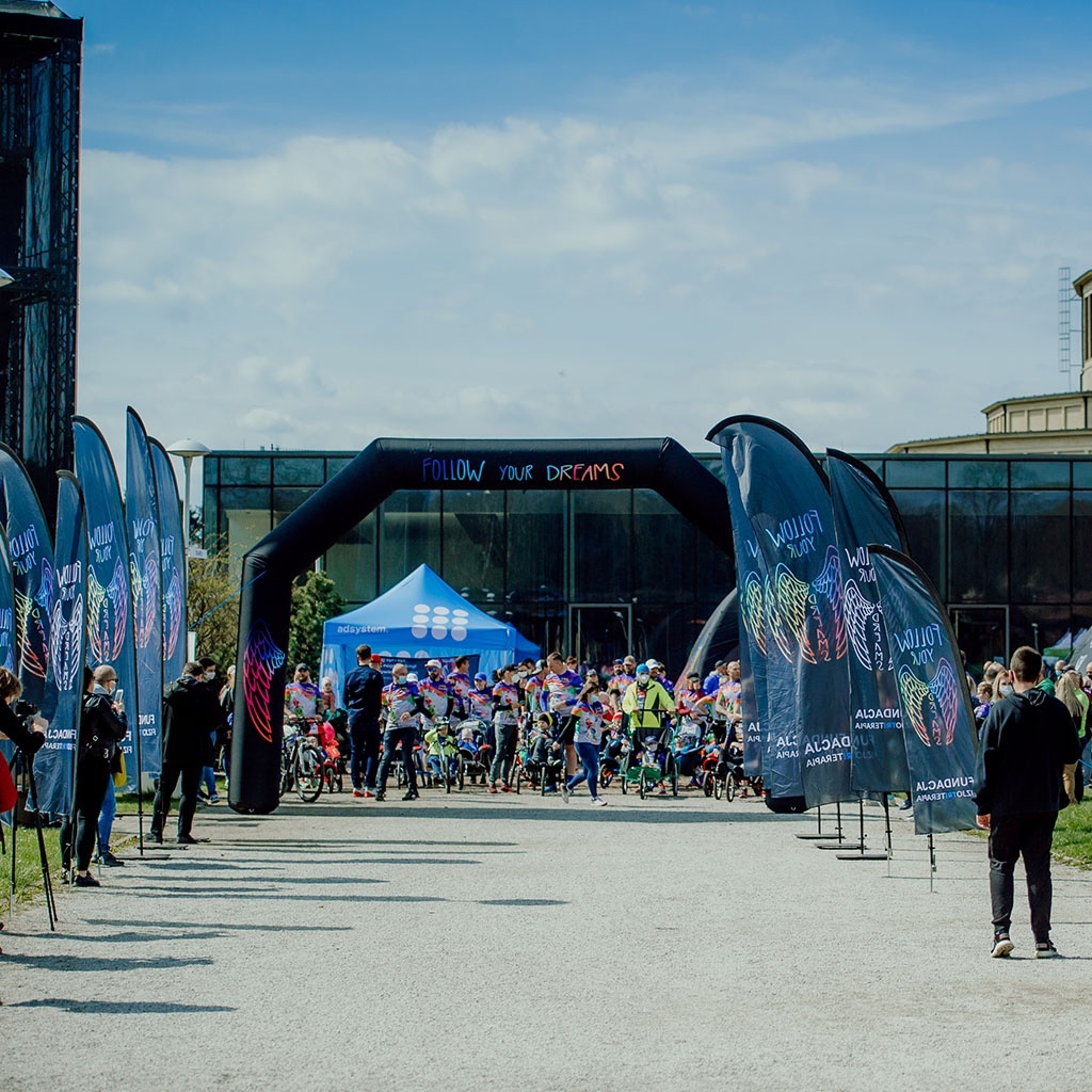 file-meta-description.outdoorsportseventwithbrandedadvertisingflags,aninflatablearch,andabluepromotionaltent,withparticipantsgatheringatthestartingzone.