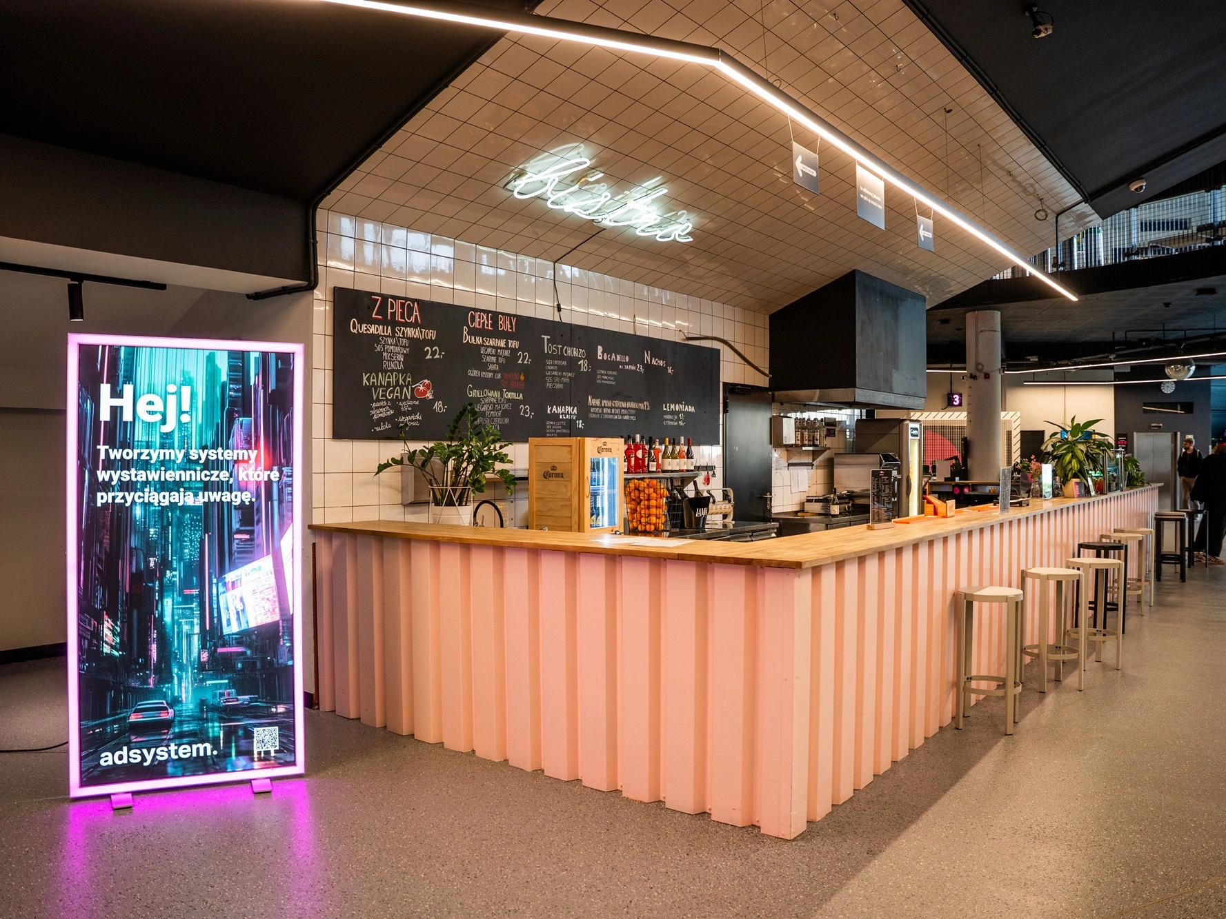Zdjęcie przedstawia podświetlaną ściankę reklamową adsystem ustawioną obok baru w przestrzeni gastronomicznej Kina Nowe Horyzonty.