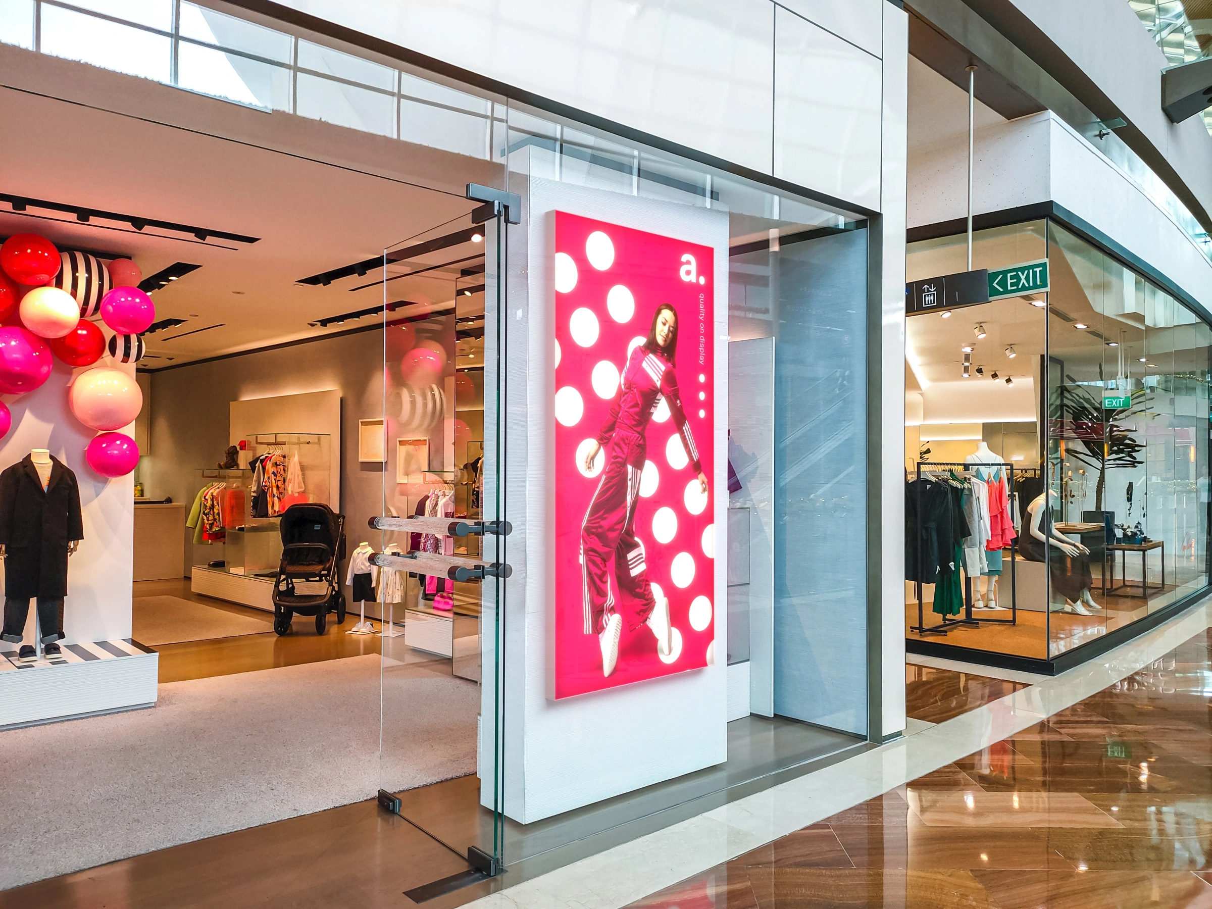 Podświetlany kaseton LED z grafiką modową zamontowany na witrynie sklepu odzieżowego w nowoczesnej galerii handlowej.