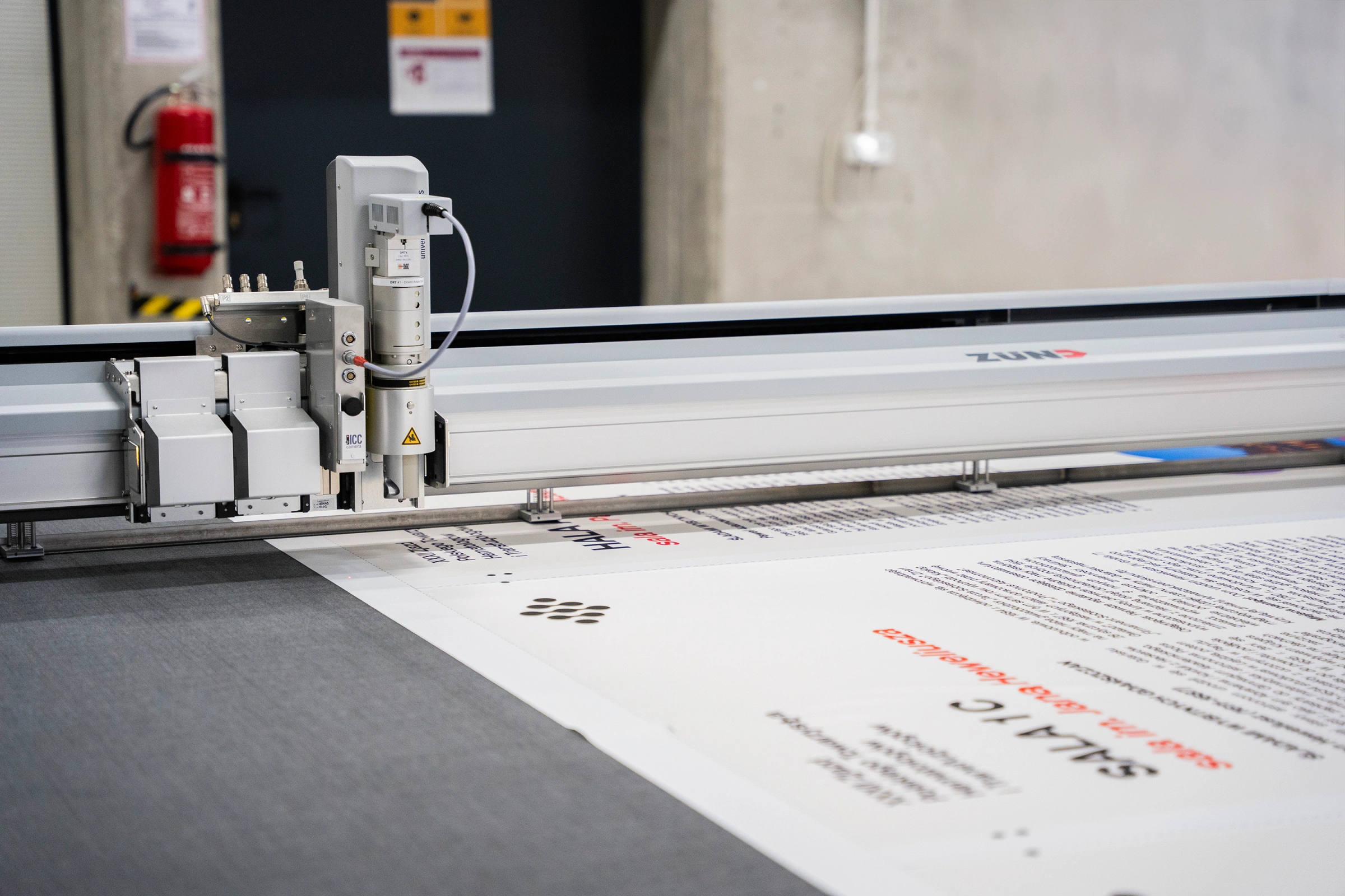 Ploter ZUND w trakcie cięcia dużego wydruku tekstylnego na stole roboczym w hali produkcyjnej adsystem.