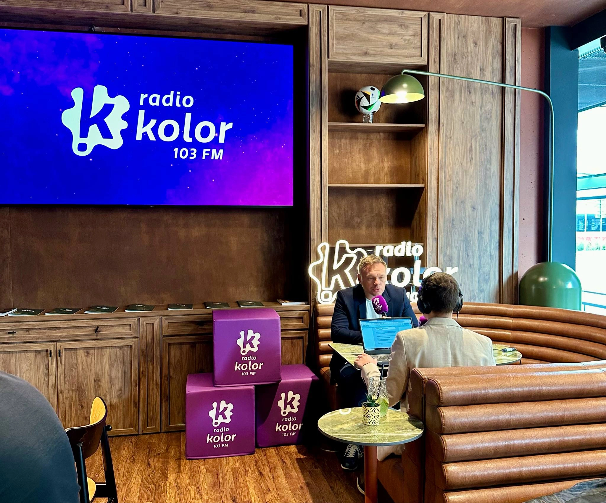 Pufy reklamowe z logo w kawiarnii. Dwie osoby prowadzą audycję radiową