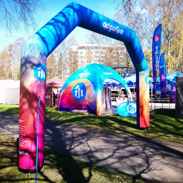 Pneumatyczna brama reklamowa i kolorowy namiot eventowy na wydarzeniu plenerowym, ustawione w parku wśród innych stoisk.